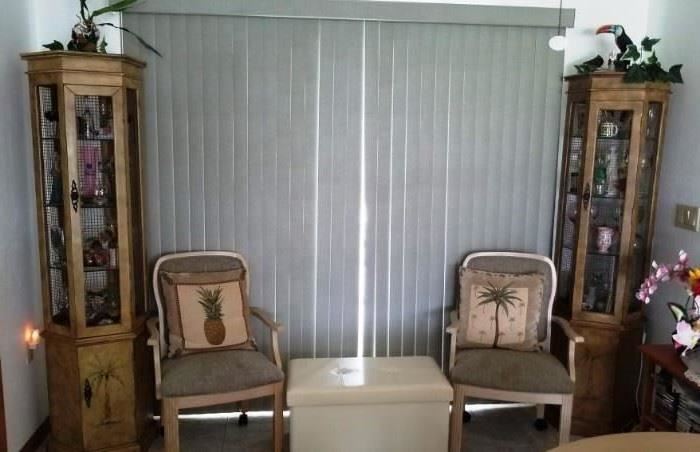 Corner lighted curio cabinets with glass shelves.  2 arm dining chairs. Tropical Palm and Pineapple throw pillows. small storage chest (appears to be faux leather/vinyl)