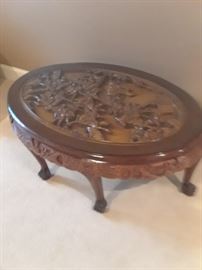 Oval coffee table with heavily carved top and glass top. Four small benches slide under table.