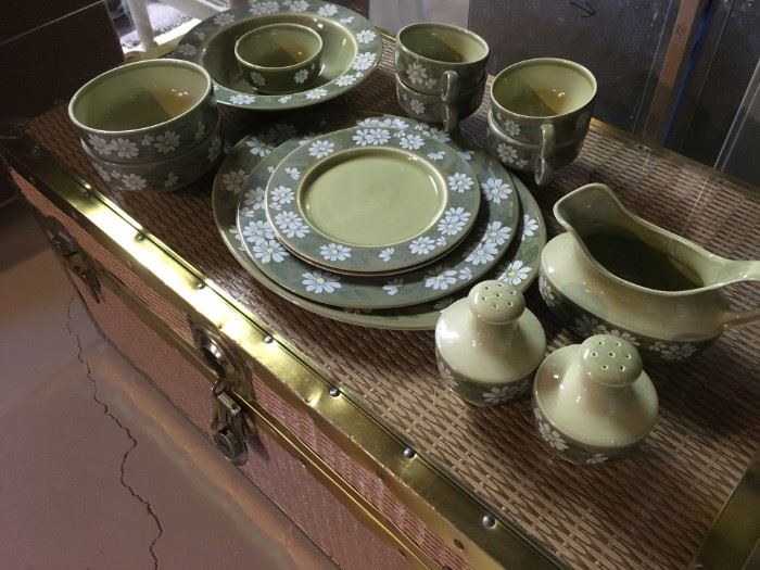 A dish set display on-top of a cedar line wicker storage chest.