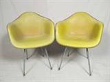 Pair of Eames design molded fiberglass armchairs produced by Herman Miller. Cushioned and covered in yellow leatherette. Well worn.