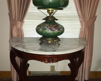 Victorian-style demi-lune table with marble top and carved wood base, floral design. (Maker unknown.)