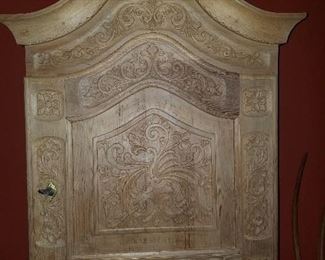 Unpainted carved wooden wall cabinet, single door with lock.