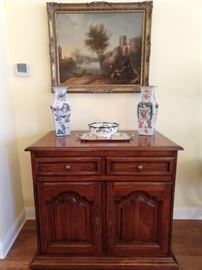 Nice pastoral scene original oil, on canvas, above a vintage repurposed mahogany cabinet, with a surprise. It has a remote control that allows the top to rise, revealing a hidden TV. Nice pair of vintage Asian porcelain vases, silverplated tray and French Limoges porcelain bowl.