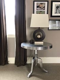 Modern silver round table, art deco lamp with rectangular lamp shade and wooden candle holder.