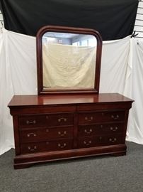 Beautiful cherry wood dresser with mirror. Crown molding top with hidden drawers. Approximate dimensions of dresser are 68" W X 20" D X 36" H. Attached mirror is approximately 39" H X 39" W. Matches lot 30 for complete set. Please bring proper help and.or equipment for removal.