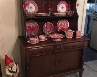 Very nice sideboard/dresser with outstanding pink and white dishes and lovely colored stems. Notice the garden gnome by the furniture piece.
