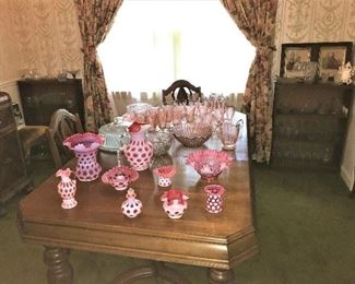 Fenton Coin Dot baskets, vases, bowls, pitcher Pink Depression glasses and pitcher. Two Bookcases in background filled with vintage glass.