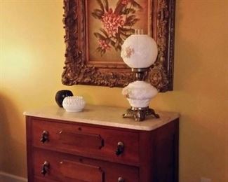 Antique three-drawer marble top chest beneath an oil painting with an ornate frame.