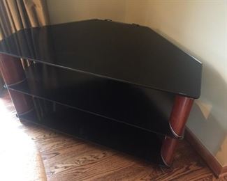 Corner TV stand.  Three smoky black glass shelves supported by  mahogany colored posts. Can be disassembled to move. 