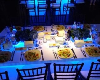 White acrylic, trapezoid-shaped dinner tables with illuminatable bases. 