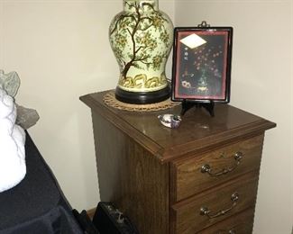 Two-drawer file cabinet with the look of nice furniture, Asian-themed lamp, wall decor.