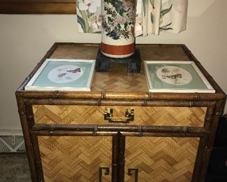 Asian-style end table with one drawer and doors below, framed butterfly prints and Asian vase.