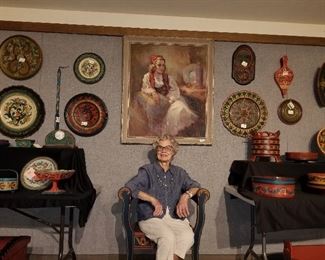 Marilynn Madden posing with her portrait seated among her collection of Norwegian rosemaling items.