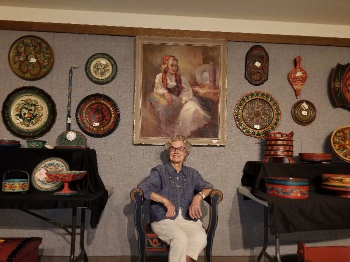 Marilynn Madden posing with her portrait seated among her collection of Norwegian rosemaling items.