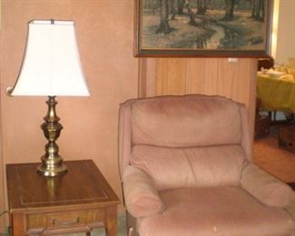 Brass table lamp, rectangular end table, large woodsy picture, tan recliner.