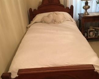 Twin size antique bed, mattress set, end table, pictures and lamp. White bedspread with pillows.