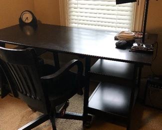 Sleek black modern desk with black office chair, desk lamp, & clock. 