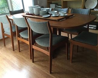 Mid Century Modern Danish Modern dining table shown with one leaf in table and one on top, with ten chairs! With the additional leaf put in they all fit around the table. Upholstery in good condition.