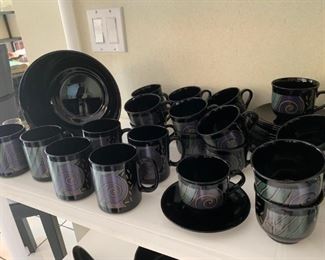 Black dinnerware set with design on the edges of plates and designs on outside of cups and bowls.