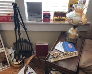 The den has it all. A tripod. Cute end table. Old fashioned lamp. Gadgets in the windowsills and more