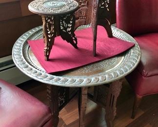 Indian carved tables atop larger table with pictoral hammered brass top