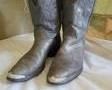 A pair of men's grey Nocona boots with pointed toes accented with a silver tone metal tip, embroidery on the toes boxes and grey and white embroidery on the shafts. They have pull straps, stacked heels. The boots are size 8.5D.

There is wear to soles, scuffs and scratches throughout, wrinkling of vamps. They appear to have much wear left.