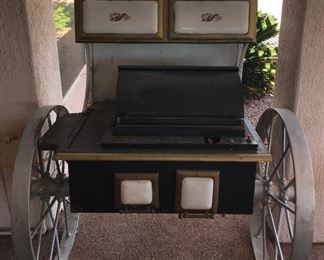 1 of a kind gas grill on wagon wheels with old cook stove for upper storage.