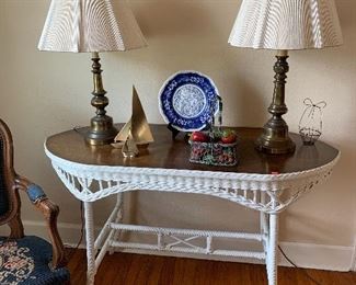 Antique wicker console table with vintage brass lamps and brass sailboats. 