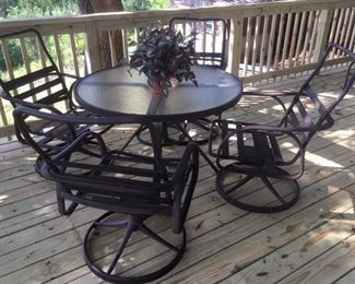Set of 4 metal swivel arm chairs with rugged fabric supports awaiting your choice of cushions; round metal table with glass top and cut out for umbrella