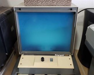 425: Datagraphic 1325 microfilm reader with storage box.
This is a Datagraphic 1325 microfilm/microfiche reader with storage box. Considered part of obsolete media, this vintage equipment was used for imprinting and storing miniaturized forms on a piece of transparent film. Circa (1960's-2000)