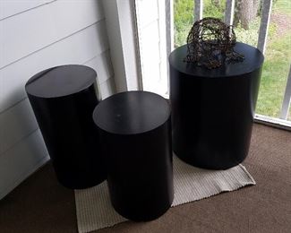 Black display cylinders, one with wire frog sculpture