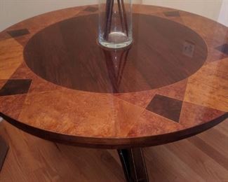 Round center table in walnut with parquetry top featuring center star in satinwood and other accents in birch and burlwood. Shaped tripartite base with gilding and black painted bases for bronze claw feet.
Underside with metal John Widdicomb label