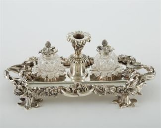 Ornate French silver plate inkstand with two cut glass and silver plate inkwells and a central chamberstick. Elaborate floral borders and flower-formed feet. C. early 20th century. One of the feet is loose. 
SKU: 01909
Follow us on Instagram: @revereauctions