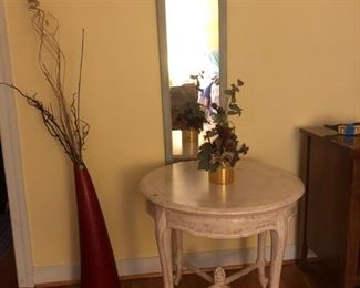 Round table, distresses white with front drawer. Antique mirror hanging on wall. Upstairs bedroom.
