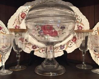 Covered glass compote. Wedgewood China in background. Crystal wine glasses with gold rims. 