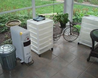 Screened Porch: An aluminum storage can with lid is near one of two HOLMES heaters, two plastic storage bins, and a metal bicycle plant stand.