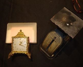 Family Room: A vintage EMES (German) wind-up alarm clock with cabriole feet, embossed rampant lion coat of arms on each side, Roman numeral dials and enameled minute and hour hands is to the left of a vintage PELOUZE postal scale.