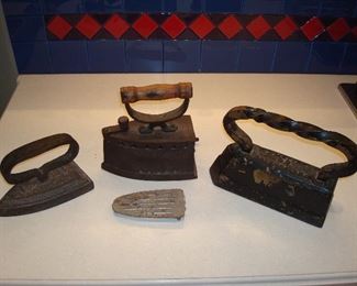 Family Room: Three antique irons left to right: 1) a flat iron; 2) a heavy charcoal iron has a wooden handle and vent holes (the trivet/stand in front actually stores inside the iron); and 3) another very heavy iron with twist handle.