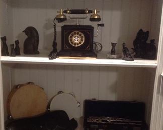 Family Room: Shelf one: vintage KODAK Brownie Fun Saver Movie Camera; a cat figure; and a vintage KODAK Tourist II camera. Shelf two: more cat figurines surround a "Thomas Collector's Edition Telephone" (it works--just plug it into a wall jack). Shelf three: a LOGITECH rechargeable speaker for Ipod & iPhone s715i with case; guitar strings; a SABINE auto tuner (for musical instruments); two tambourines; a vintage ARMSTRONG Cadet flute in case; and several recorders (including one Yamaha).