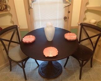 Kitchen: Two RESTORATION HARDWARE black metal "x" back chairs are shown. The one on the left shows a chair with a pad while the one on the right has the pad removed so you can see the perforated metal seat. The heavy 40" round iron pedestal table displays six pink cabbage leaf plates and a white opaque vase.