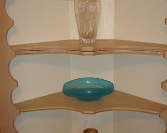Kitchen: The second built-in corner display cabinet shows a heavy crystal etched vase a decorative blue bowl, two white bowls, an amber candle holder, and six clear square dinner plates.