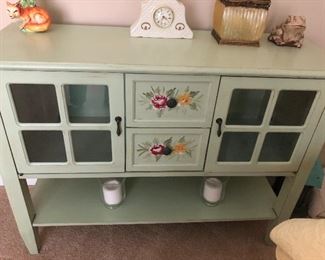 pretty narrow storage cabinet painted with poisonous plants, also a clever ceramic fox, a clock, luminescent carnival class vase and confused frog