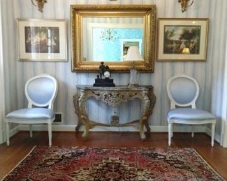 Beautiful foyer, with hand woven Persian rug, pair of silk covered French side chairs, hand painted wooden console, pair of vintage Italian gold gilt 2-light wall sconces, unbelievable gold gilt wall mirror, gold gilt wooden wall sconce, with vintage pottery vase.