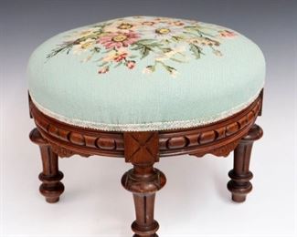 Lot 25: A 19th Century Victorian Walnut Footstool.  Floral needlework top, circular carved skirt, four turned legs.  Older finish with some wear.  18" diameter, 14" high.