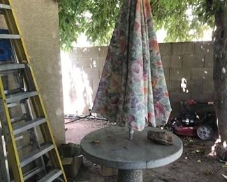 CONCRETE TABLE WITH UMBRELLA. ALSO, LADDERS AND TWO LAWN MOWERS.