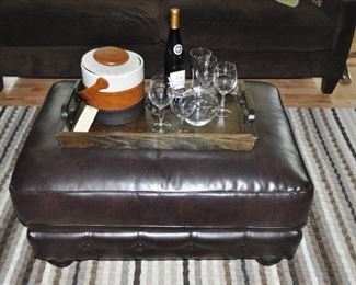 Dark brown leather ottoman, 36.5”w x 17”h x 26.5”d  Shown with large wood serving tray, Riedel bar ware and vintage ice bucket. 