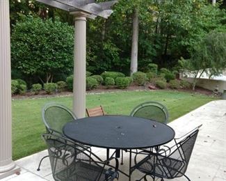 One of two outdoor wrought iron patio tables with four armchairs.