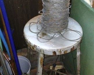 Vintage painted metal shop stool and roll of vintage barbed wire.