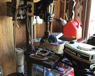 . . . this is a neat vintage drill press next to a Sears Game Fisher vintage boat motor.