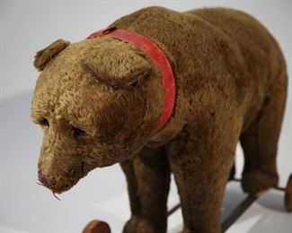 Large toy riding bear on metal platform with wooden wheels. Red collar, red ribbon around body and glass eyes. circa 1885.